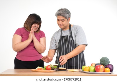 Happy Overweight Couple Cooking A Burger In The Kitchen Room. A Vegetable On The Table. Concept Of Happy Family And Binge Eating