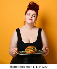 Happy overweight fat woman happy hold big burger cheeseburger sandwich with beef in hand laughing on yellow background. Girl on diet dieting. Healthy eating  fast food concept