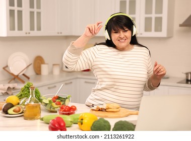 Happy Overweight Woman With Headphones Dancing While Cooking In Kitchen