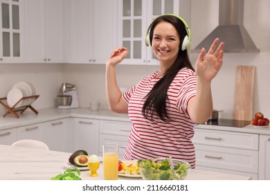 Happy Overweight Woman With Headphones Dancing Near Table In Kitchen. Healthy Diet