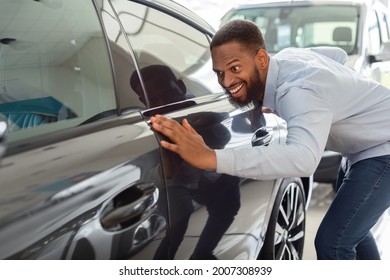 Happy Owner. Excited Black Man Touching His New Car In Showroom After Buying, Overjoyed African American Guy Purchase Automobile In Dealership Salon, Looking At Surface Of New Vehicle, Closeup Shot