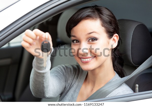 Happy owner of a new car is showing the car key.\
Pretty girl driver