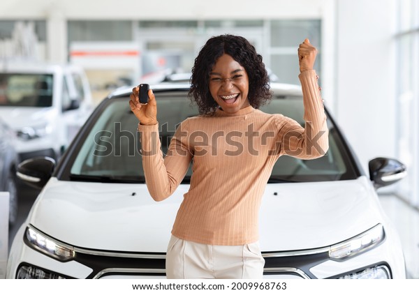 Happy Owner. Overjoyed Black Lady Holding Keys Of\
Her New Car After Buying, Cheerful African American Woman Standing\
Near Vehicle In Dealership Center And Raising Fist With Excitement,\
Copy Space
