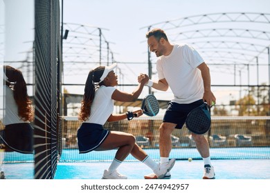 Happy paddle tennis player helping his female partner to get up on the court. - Powered by Shutterstock