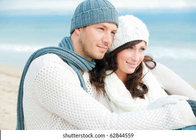 Happy Pair Of Male And Female Embracing And Having Fun Wearing Warm Clothes Outside On Coast Behind Blue Sky