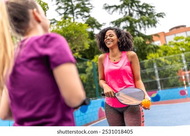 Happy pair of multi-ethnic women playing pickelball in an outdoor court - Powered by Shutterstock