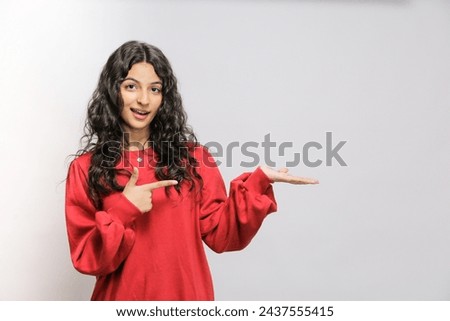 Happy Pakistani girl showing product. Beautiful Pakistani girl with curly hair pointing to side .Presenting your product. Isolated on white background. Expressive facial expressions