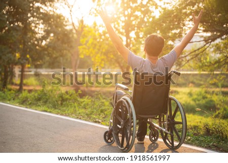 Happy Paralyzed,disabled or handicapped man in hope sitting relax on a wheelchair in nature park.Disabled handicapped man has a hope use smart phone for working,calling and searching for social media