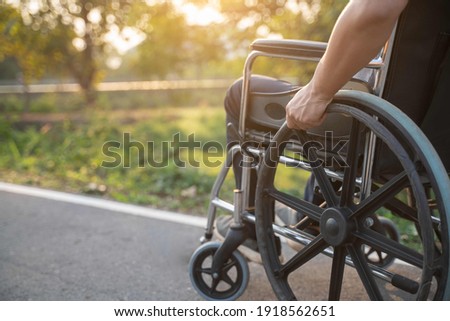 Happy Paralyzed,disabled or handicapped man in hope sitting relax on a wheelchair in nature park.Disabled handicapped man has a hope use smart phone for working,calling and searching for social media