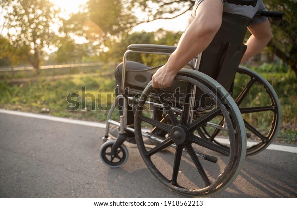 Happy Paralyzed,disabled or handicapped man in hope\
sitting relax on a wheelchair in nature park.Disabled handicapped\
man has a hope use smart phone for working,calling and searching\
for social media