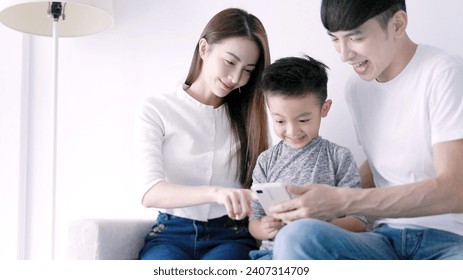 Happy parent and  kid using mobile phone, resting on home couch together