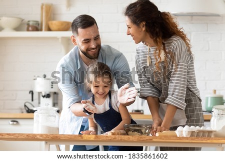 Happy parents with adorable little daughter having fun with dough, baking pastry or pie together, laughing father clapping hands with flour, overjoyed family enjoying leisure time in kitchen