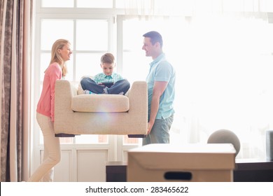 Happy parents carrying son on armchair in new house