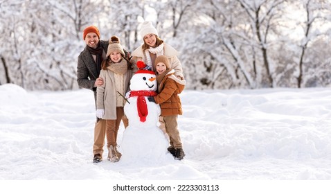 Happy parents and children gathering in snow-covered park together sculpting funny snowman from  snow. Father, mother and two kids playing outdoor in winter forest. Family active holiday - Powered by Shutterstock