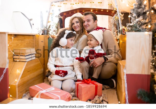 Happy parents and\
children with gift boxes in their hands in red car in pickup\
trailer near Christmas\
tree.