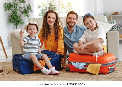 Happy parents with children laughing at camera while sitting on floor near sofa with suitcases near at home