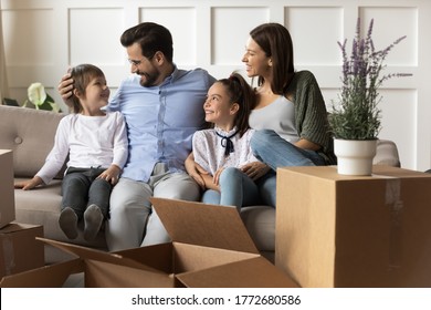 Happy parents with children relaxing on sofa on moving day, smiling father and mother with little son and daughter sitting on couch in living room with cardboard boxes, relocation and mortgage