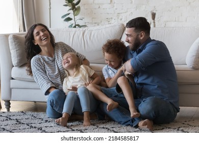 Happy parents cuddling, tickling little children on floor, laughing, having fun, enjoying family activity, leisure. Cheerful excited mom and dad playing with giggling son and daughter kids at home