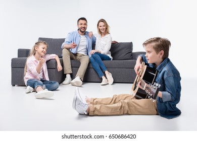 Happy parents and cute little sister looking at smiling boy playing guitar  - Powered by Shutterstock