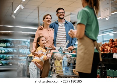 Happy parents with daughter buying groceries and communicating with supermarket worker at the store. - Shutterstock ID 2279180185