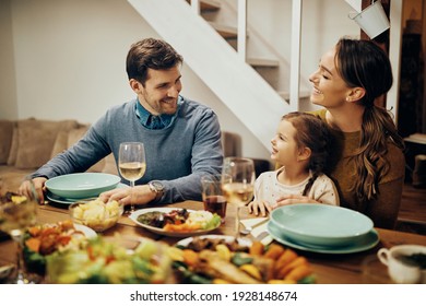 Happy parents with daughter enjoying in conversation during a meal at dining table.