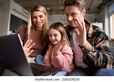 Happy Parents And Daughter Having Family Video Call Using Laptop At Home. Family With Kid Waving Hands Looking At Computer At Home Having Virtual Online Conversation Together In Living Room.