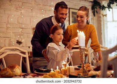 Alegres padres con sus hijas encendiendo velas en menorah en la mesa mientras celebraban Hanukkah en casa.