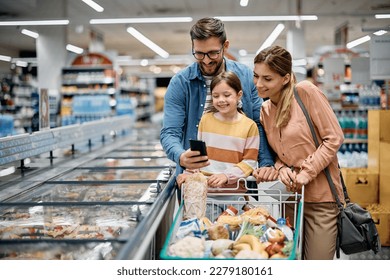 Happy parents with daughter using app on cell phone while buying groceries in the supermarket. Copy space. - Powered by Shutterstock