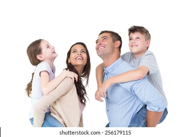 Happy Parents Giving Piggyback Ride To Children While Looking Up Over White Background