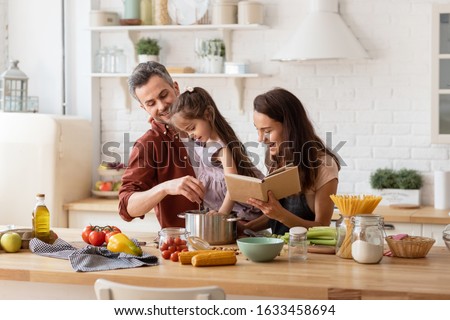 Happy parents helping daughter to cook. Mother with cookbook in hand, father with child on hand watching girl trying to catch something in pan. Family recreation and fun, loving relationships