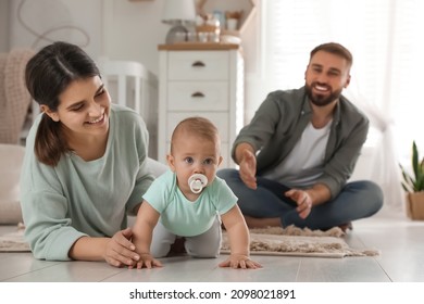 Happy Parents Helping Their Baby To Crawl On Floor At Home