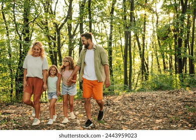 A happy parents are holding hands with their daughters and taking a walk in forest. An active loving family is spending day in nature together. Portrait of active family hiking in forest on sunny day. - Powered by Shutterstock