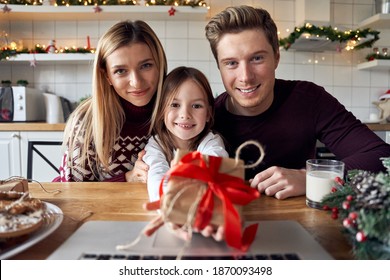 Happy Parents Hugging Cute Small Kid Daughter Holding Present Giving Christmas Gift To Web Camera During Virtual Family Social Meeting On Video Conference Call Party At Home, Laptop Webcam View.