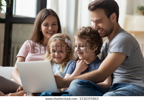 Happy parents with little daughter and son using laptop, sitting on