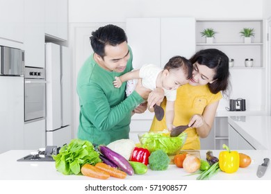 Happy Parents And Little Girl Making Salad Together While Standing In The Kitchen 