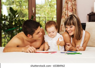 Happy parents playing and their little daughter at bedroom