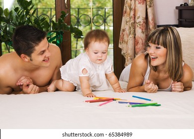 Happy parents playing and their little daughter at bedroom