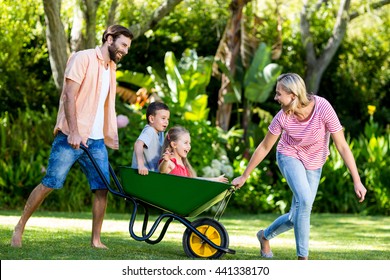 Happy parents pushing children sitting in wheelbarrow at yard