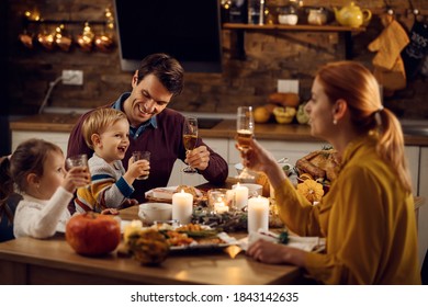 Happy Parents With Small Kids Toasting And Having Fun During Thanksgiving Meal In Dining Room.