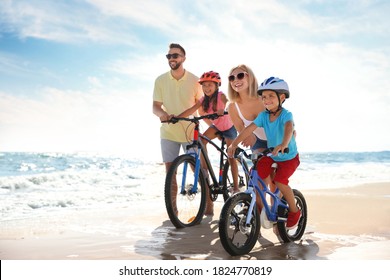 Happy parents teaching children to ride bicycles on sandy beach near sea - Powered by Shutterstock