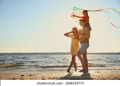Happy parents and their child playing with kite on beach near sea. Spending time in nature