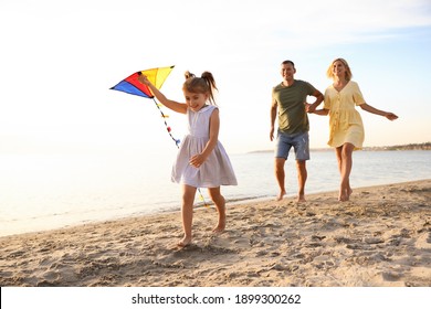 Happy parents with their child playing with kite on beach. Spending time in nature - Powered by Shutterstock