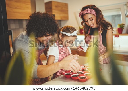 Happy parents and their daughter are preparing cookies together in the kitchen. Little girl helps to her parents to put crumbs of chocolate on the cookies.