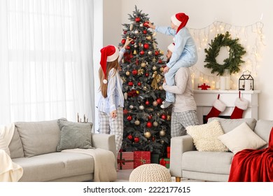 Happy parents with their little son in Santa hats decorating Christmas tree at home