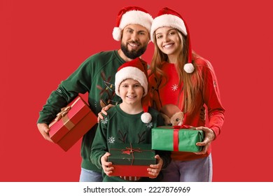 Happy parents with their little son in Santa hats and Christmas gifts on red background - Powered by Shutterstock