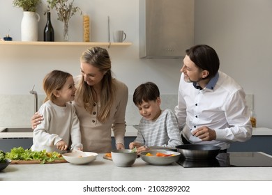 Happy Parents And Two Sibling Kids Preparing Lunch, Dinner Together, Cooking Healthy Meal From Natural Ingredient, Slicing Salad, Heating Frying Pan, Talking, Laughing, Having, Fun