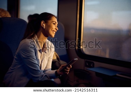 Happy passenger enjoying in view through the window at sunset while commuting by train.