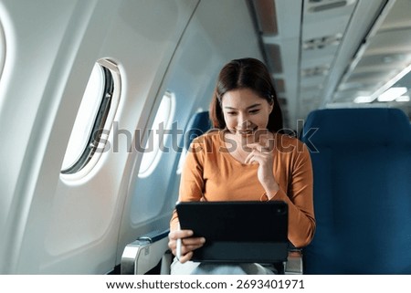 Happy passenger using digital tablet while traveling by airplane, enjoying entertainment during air travel
