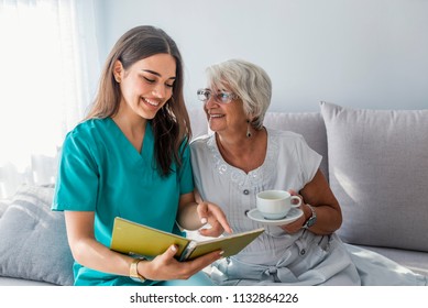 Happy patient is holding caregiver for a hand while spending time together. Elderly woman in nursing home and nurse. Aged elegant woman and tea time at nursing home