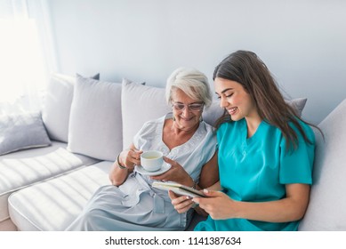 Happy Patient Is Holding Caregiver For A Hand While Spending Time Together. Elderly Woman In Nursing Home And Nurse. Aged Elegant Woman And Tea Time At Nursing Home